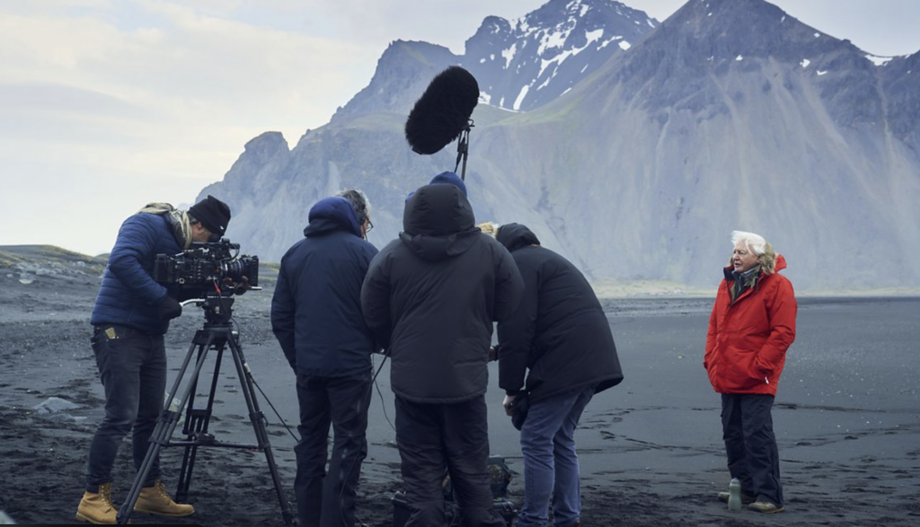 Film crew filming a man in front of large mountains